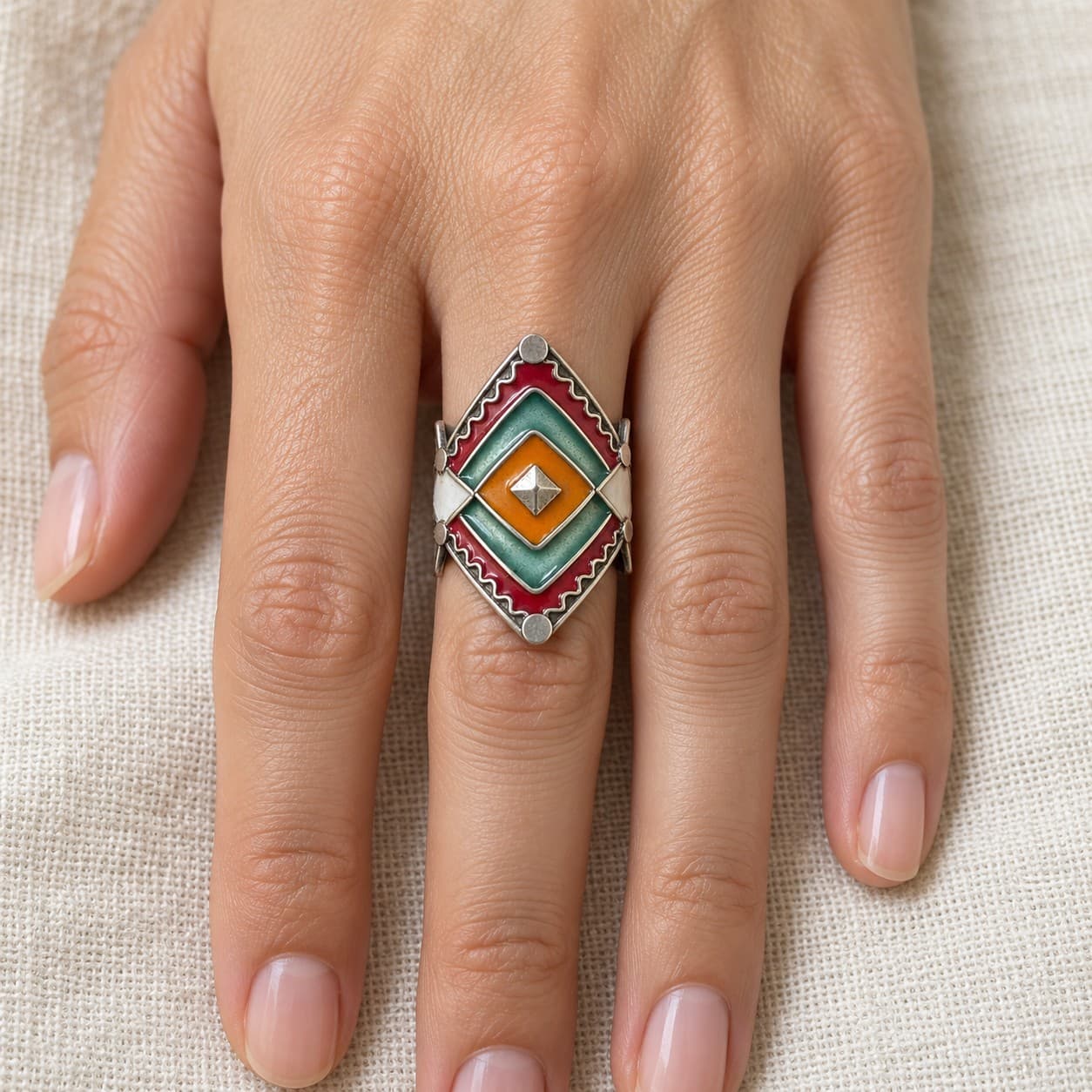 Bague MINA en argent émaillé portée à la main, motif en losange rouge, vert et orange